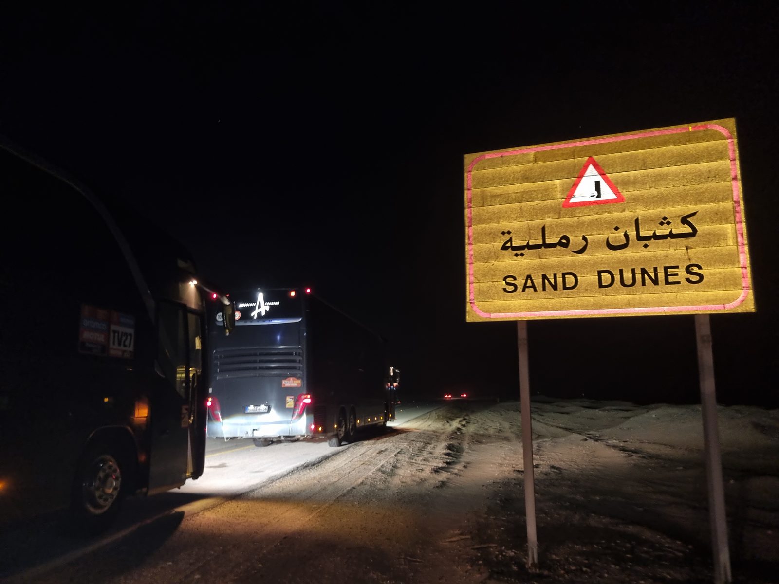 Busse bei Nacht vor Sanddünen-Warnschild in Saudi-Arabien